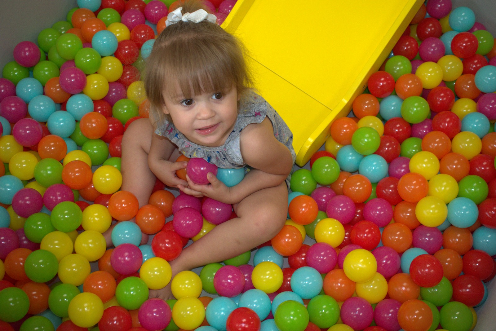Young girl exploring the indoor sandbox at Kiddie Kingdom while playing with a plastic toy.